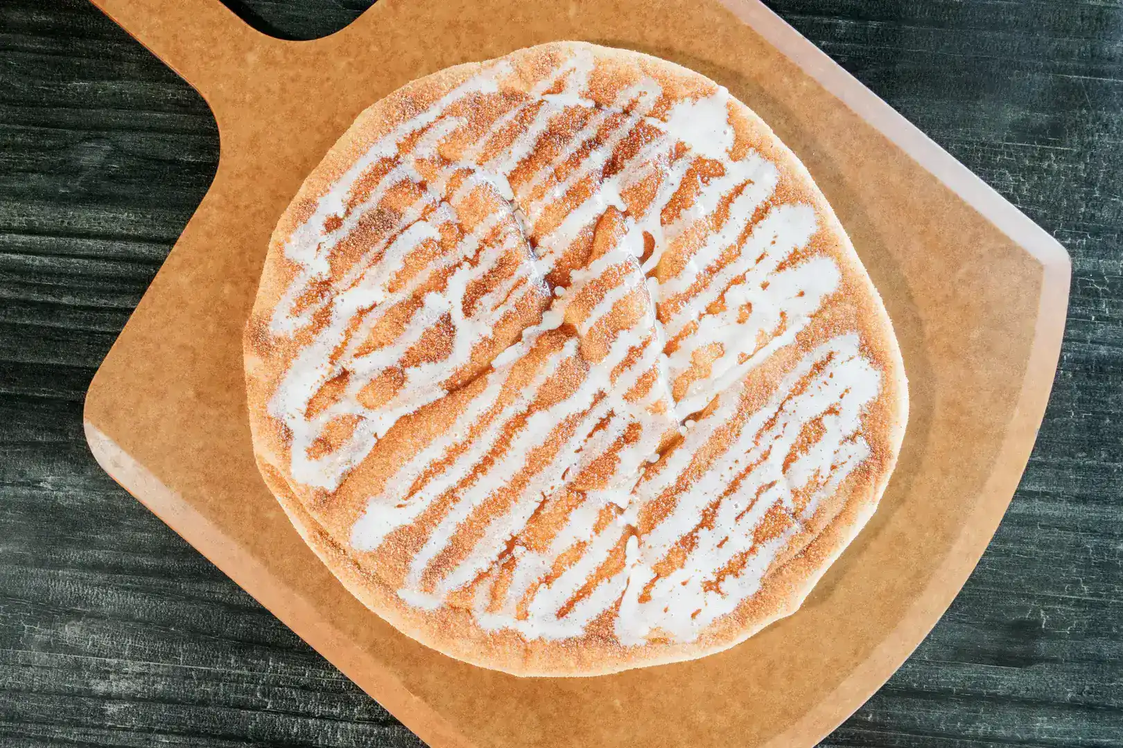 Close-up of a Sicilian pizza with white drizzle on a brown paper.